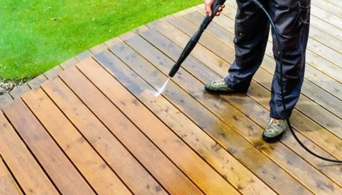 Person pressure washing a wooden deck outdoors.