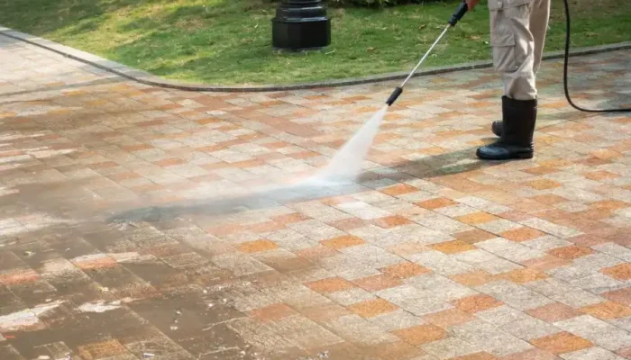 Person pressure washing a brick pathway outdoors.