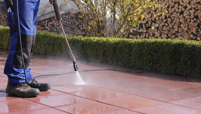 Person power washing a red stone patio outdoors.