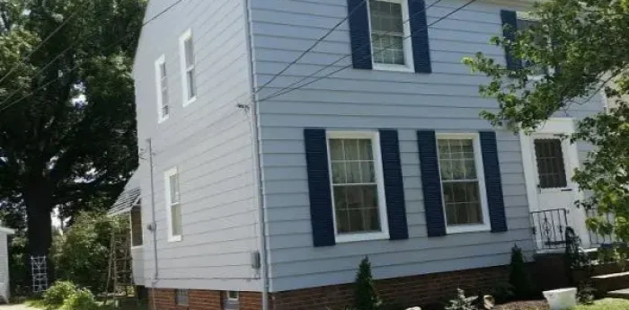 A two-story white house with blue shutters and a small garden.