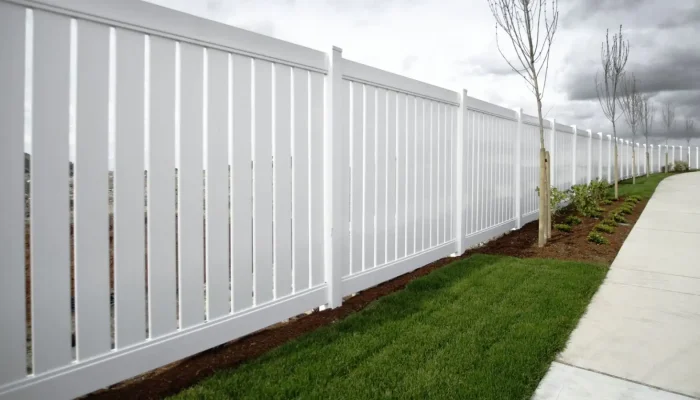 A white vinyl fence on green grass under an overcast sky.